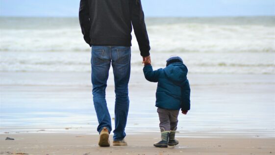 man and boy walking on seashore under blue sky