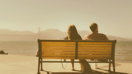 man and woman sitting on bench beside body of water