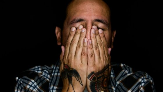 man wearing black, white, and gray plaid sport shirt covering his face