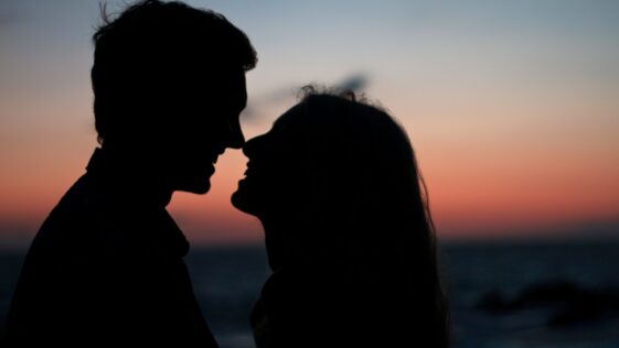 silhouette of man and woman about to kiss on beach during sunset