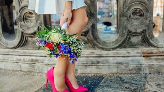 woman holding white, blue, and red petaled flower bouquet beside gray concrete fence