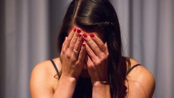 woman in black tank top covering her face with her hands
