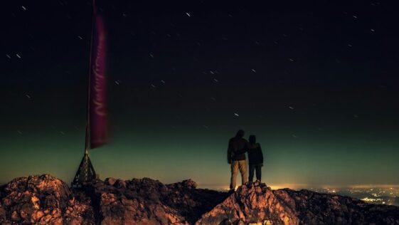 silhouette of two people standing on brown rocks under starry night