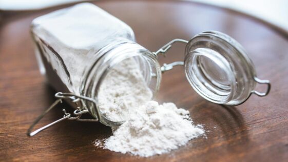 Glass jar tipped over with white flour spilling onto a wooden surface, ideal for baking themes.
