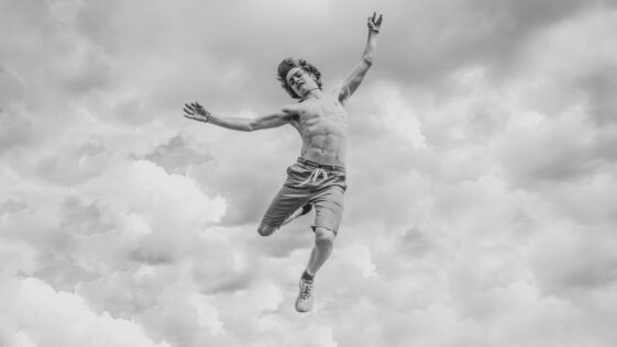 grayscale photo of person jumping overlooking clouds
