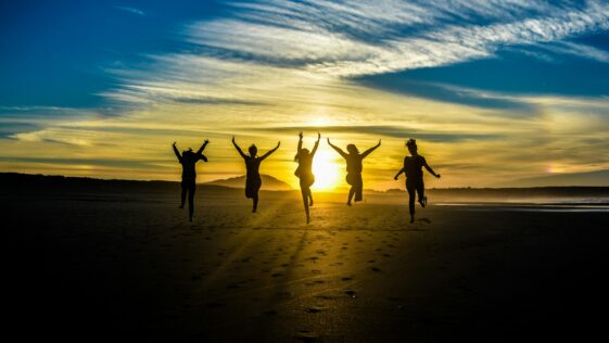 people jumping on shore front of golden hour