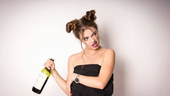 woman in black spaghetti strap top holding green glass bottle