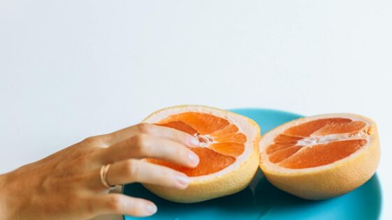 A hand gently touches grapefruit halves on a blue plate, symbolizing intimacy and freshness.