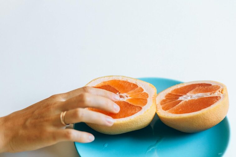 A hand gently touches grapefruit halves on a blue plate, symbolizing intimacy and freshness.