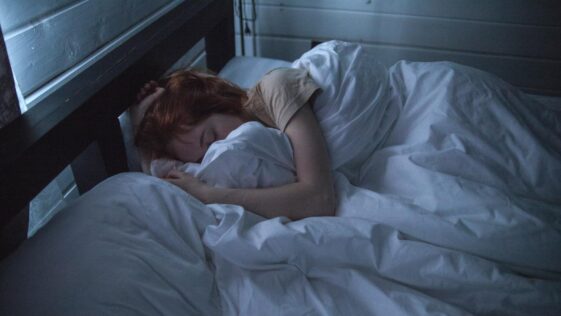 A woman sleeping peacefully in a cozy bedroom, enveloped by soft white sheets, under the gentle glow of night lighting.