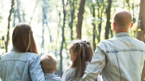 man and woman holding hands together with boy and girl looking at green trees during day