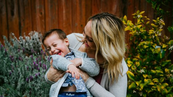 woman in gray sweater carrying baby in blue and white shirt