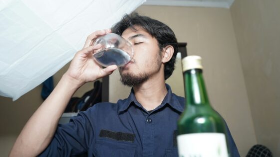 A man drinking from a wine glass next to a bottle