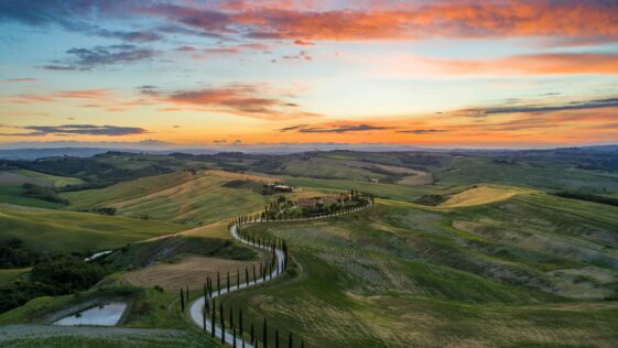 road between green grass field near mountains under blue and brown sky at golden hour