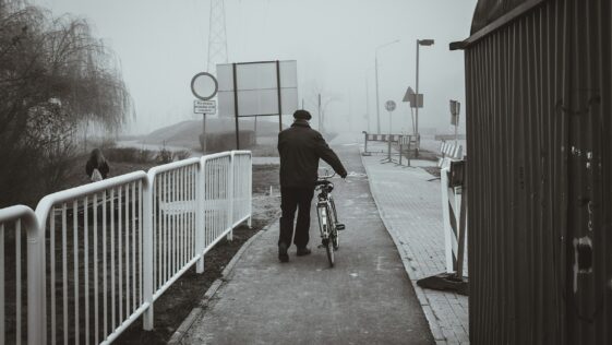 a man walking a bike down a sidewalk on a foggy day