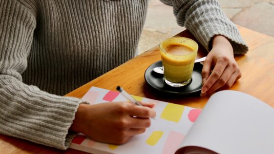 person holding pen with coffee on table