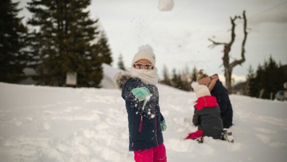 girl in pink jacket and pink pants standing on snow covered ground during daytime