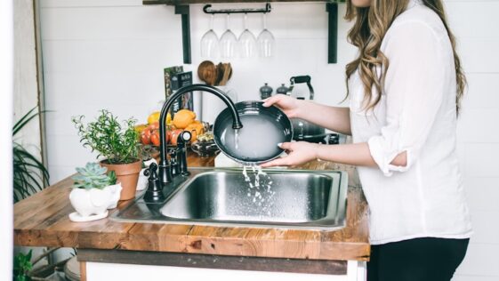 woman wearing white blouse washing dish on the faucet