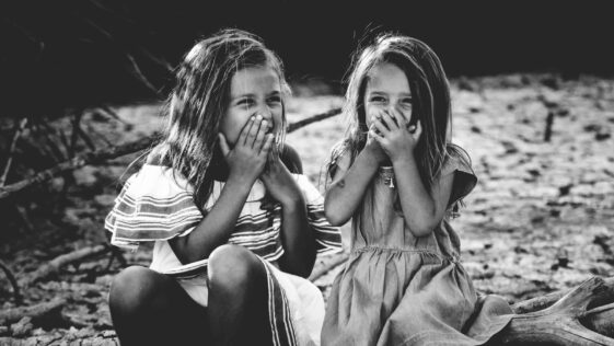 grayscale photography of two girls closing their mouths