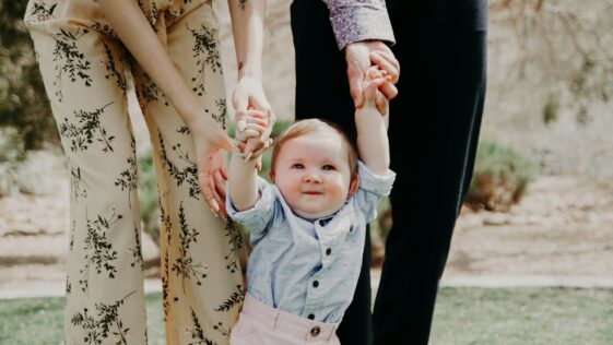 man and woman holding hand of toddler walking on grass field