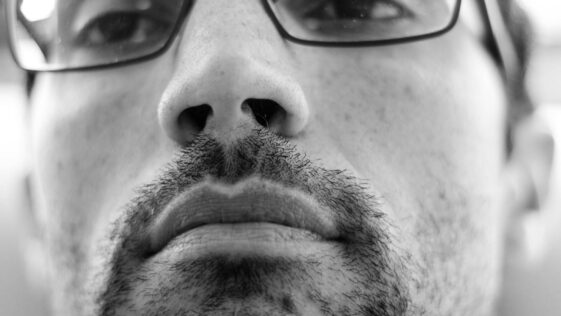 Black and white close-up photo of a bearded man wearing glasses, looking thoughtful.