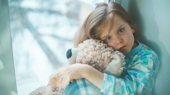 girl in blue white and red plaid shirt hugging brown teddy bear