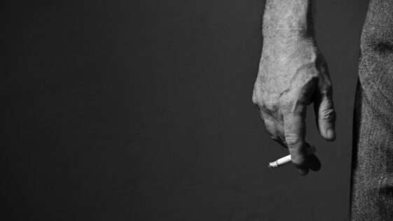 grayscale photo of person's right hand with lighted cigarette