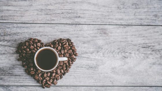 coffee filled white ceramic mug beside brown coffee beans on beige wooden surface