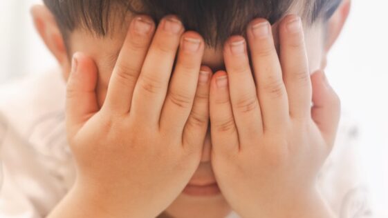 a young boy covering his eyes with his hands