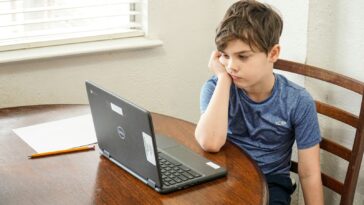boy in blue crew neck t-shirt using macbook pro on brown wooden table